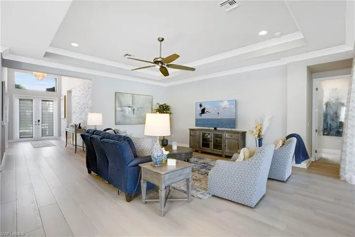 Living area featuring visible vents, ceiling fan, light wood-style floors, a tray ceiling, and french doors