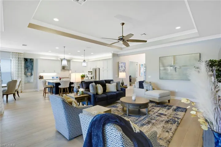 Living area with a ceiling fan, a raised ceiling, ornamental molding, and light wood finished floors