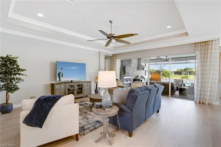Living room featuring a ceiling fan, a raised ceiling, and light wood-style flooring