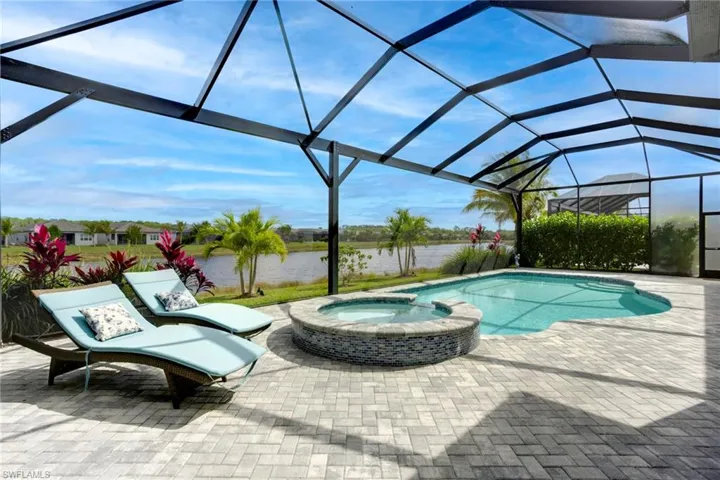 View of swimming pool featuring a pool with connected hot tub, a water view, glass enclosure, and a patio