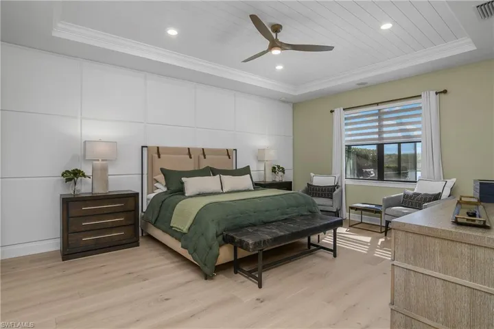 Wake up to stunning views of the lake in the primary bedroom which is spacious and features custom accent wall, newly installed hardwood flooring, coffered ceiling with tongue and groove wood accent and crown molding.