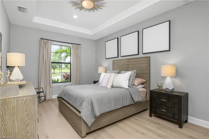 Guest bedroom includes tray ceiling with crown molding, newly installed hardwood flooring, and designer lighting.
