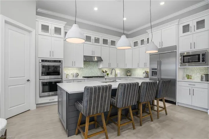Kitchen features oversized island, walk-in pantry with custom shelving, upper glass cabinets, quartz countertops, professional grade stainless steel appliances with natural gas.