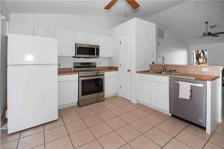 Kitchen featuring lofted ceiling, stainless steel appliances, a ceiling fan, white cabinetry, and light tile patterned floors