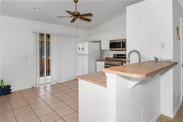 Kitchen with appliances with stainless steel finishes, a peninsula, light tile patterned floors, vaulted ceiling, and white cabinetry