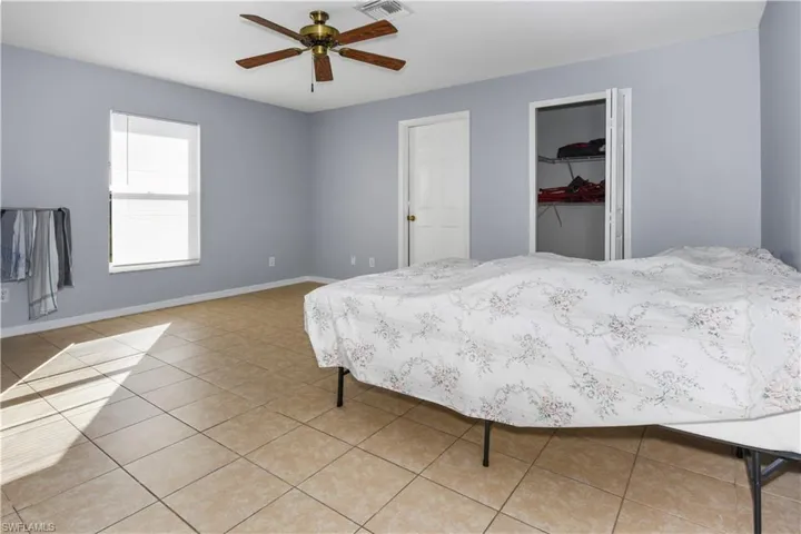 Bedroom with ceiling fan, light tile patterned floors, and a walk in closet