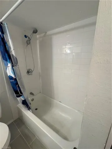 Bathroom featuring shower / bathtub combination with curtain, tile patterned floors, and toilet