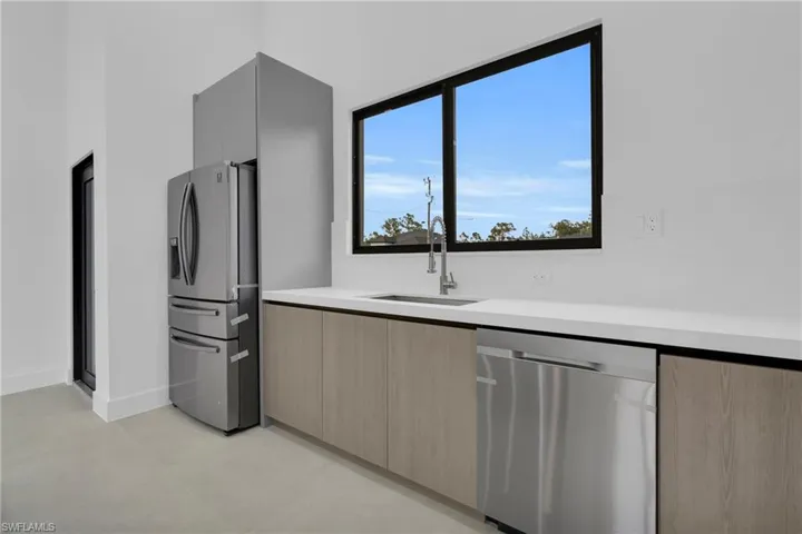 Kitchen featuring modern cabinets, stainless steel appliances, light brown cabinetry, and light stone counters