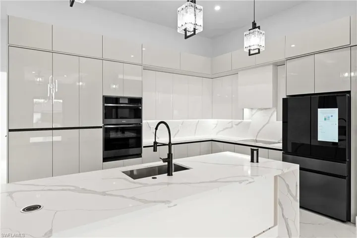 Kitchen with sink, white cabinets, hanging light fixtures, black fridge, and light stone countertops