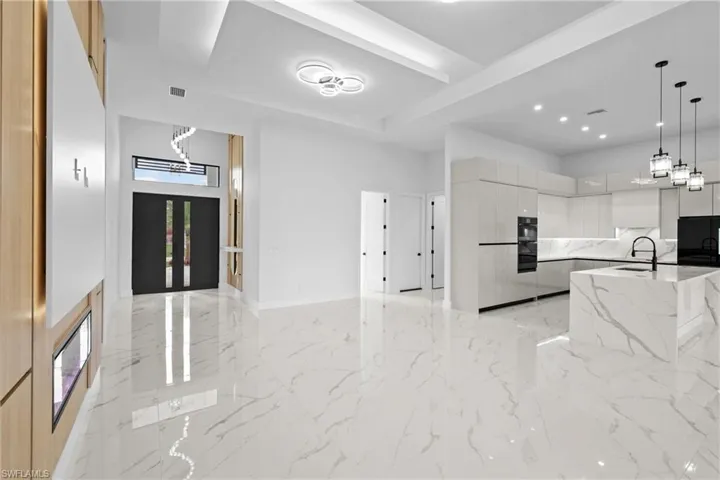 Kitchen featuring sink, white cabinetry, light stone counters, black fridge, and decorative light fixtures