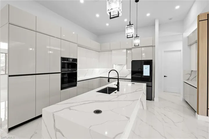 Kitchen featuring pendant lighting, double oven, white cabinetry, sink, and a large island with sink