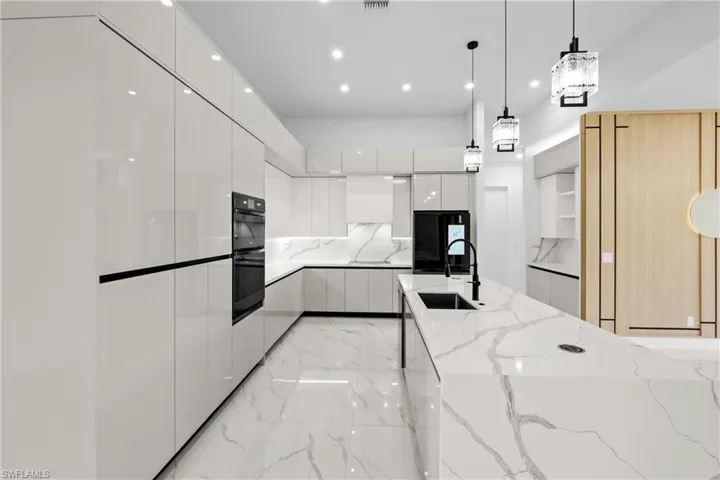 Kitchen with sink, white cabinetry, light stone counters, decorative light fixtures, and black appliances
