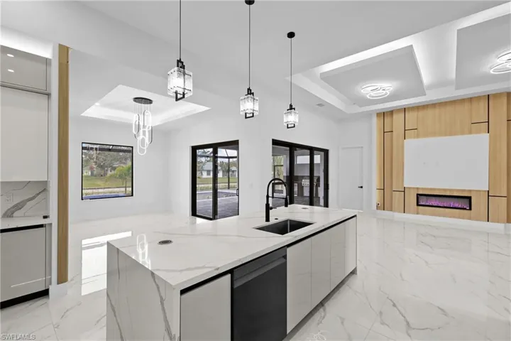 Kitchen with a spacious island, decorative light fixtures, a raised ceiling, and sink