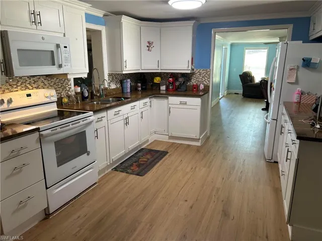 Kitchen featuring white appliances, white cabinets, light wood-style flooring, ornamental molding, and dark stone countertops