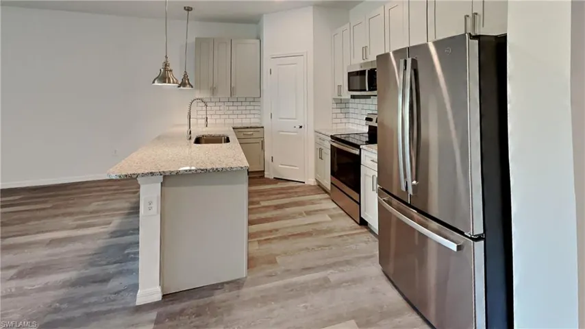 Kitchen with stainless steel appliances, decorative light fixtures, light stone countertops, a peninsula, and light wood-type flooring