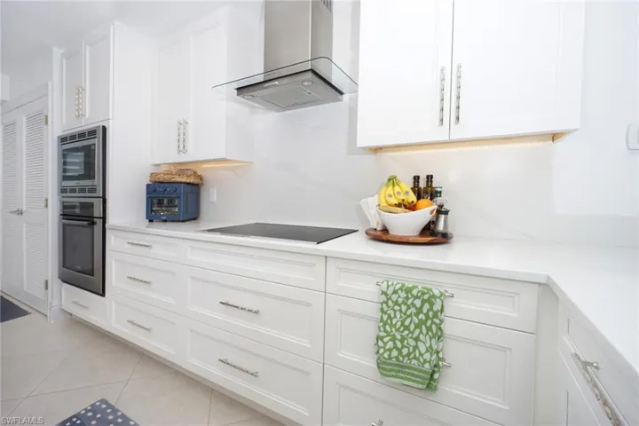 Kitchen featuring white cabinets, wall chimney range hood, appliances with stainless steel finishes, and light tile patterned floors