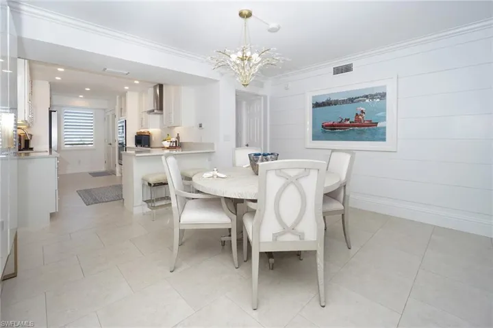 Dining area with a chandelier, light tile patterned flooring, wooden walls, and ornamental molding