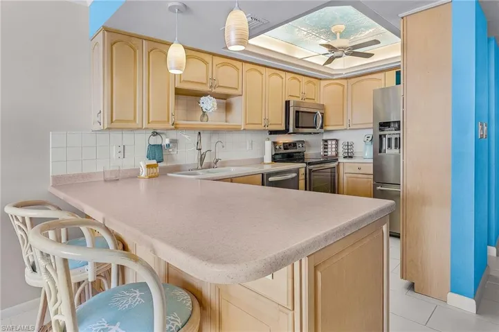 Kitchen featuring light brown cabinets, tasteful backsplash, a peninsula, stainless steel appliances, and light countertops