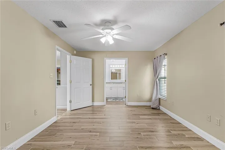 Unfurnished bedroom featuring wood finish floors, a ceiling fan, a textured ceiling, and ensuite bathroom