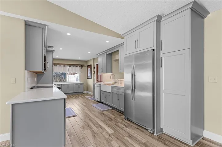 Kitchen featuring gray cabinets, stainless steel appliances, light stone countertops, light wood-style floors, and recessed lighting