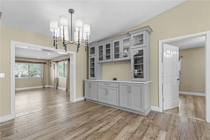 Kitchen featuring gray cabinetry, glass insert cabinets, light countertops, light wood-type flooring, and hanging lights