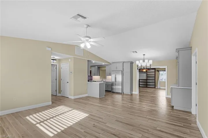 Unfurnished living room featuring hanging lights, ceiling fan, vaulted ceiling, and light wood-style flooring