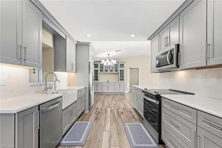 Kitchen with gray cabinets, lofted ceiling, stainless steel appliances, tasteful backsplash, and light wood-style flooring