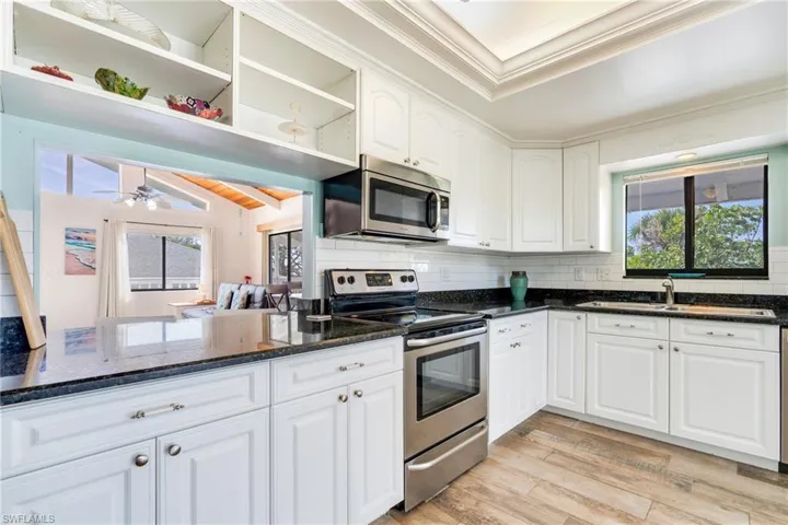Kitchen with open shelves, tasteful backsplash, appliances with stainless steel finishes, a sink, and light wood-type flooring