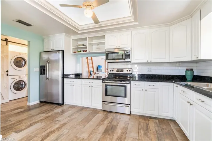 Kitchen with a barn door, visible vents, stacked washer and clothes dryer, a tray ceiling, and stainless steel appliances