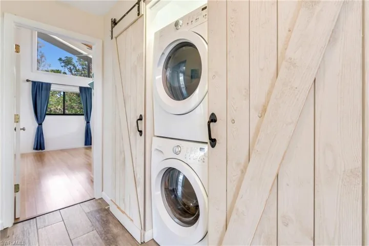 Washroom with stacked washing maching and dryer, a barn door, laundry area, and light wood finished floors