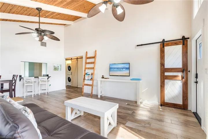 Living room with stacked washer and dryer, a ceiling fan, wooden ceiling, and a barn door