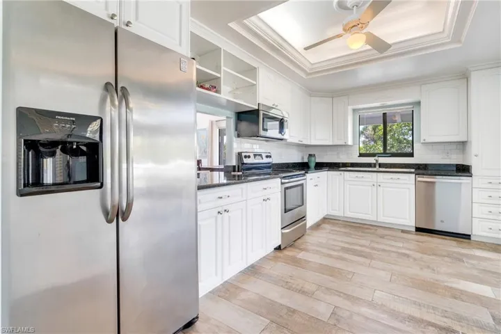 Kitchen with a raised ceiling, a sink, stainless steel appliances, light wood-style floors, and backsplash