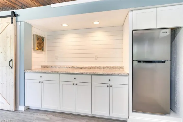 Kitchen featuring light stone countertops, a barn door, white cabinets, and freestanding refrigerator