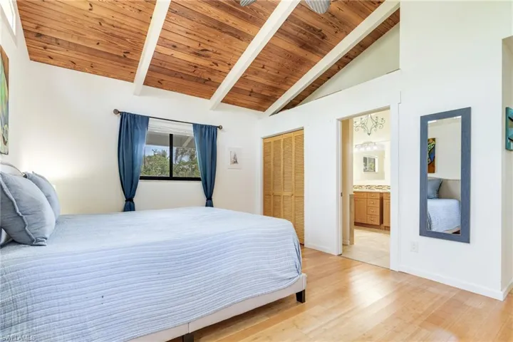 Bedroom with wooden ceiling, light wood-style flooring, connected bathroom, and beam ceiling