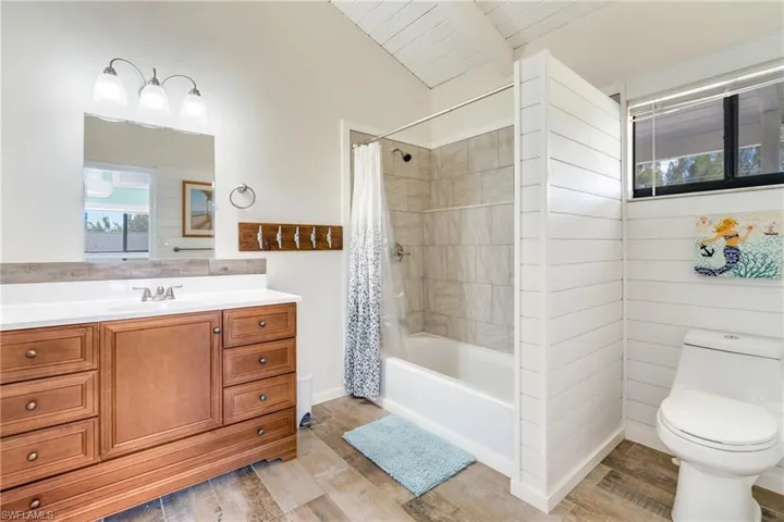 Full bathroom featuring vaulted ceiling with beams, toilet, shower / bath combo, vanity, and wood finished floors