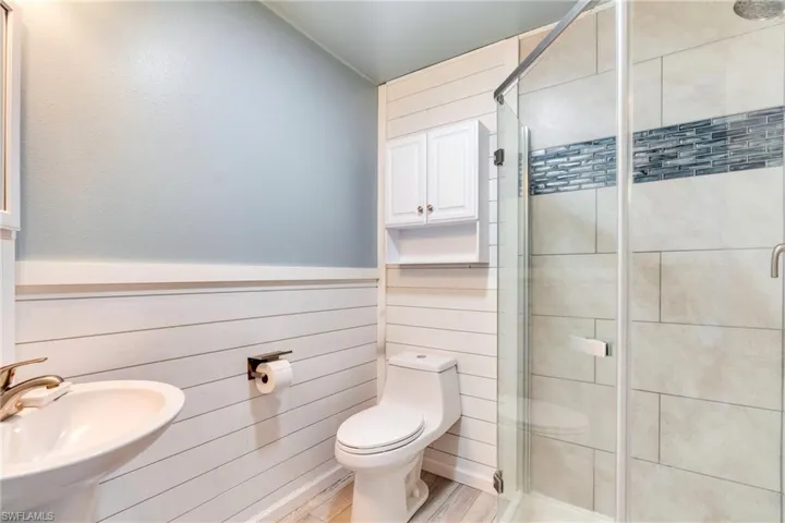 Bathroom featuring a stall shower, wooden walls, toilet, a wainscoted wall, and a sink