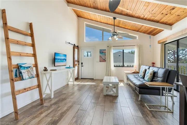 Living area featuring a barn door, baseboards, a ceiling fan, wood finished floors, and beam ceiling