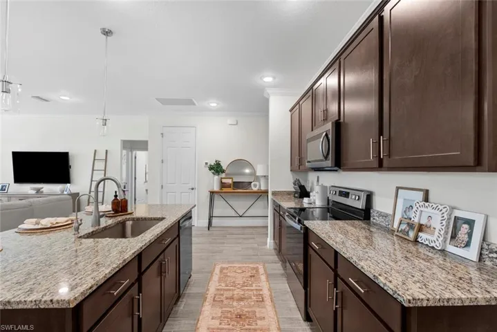 Kitchen featuring stainless steel appliances, an island with sink, sink, light hardwood / wood-style floors, and light stone counters