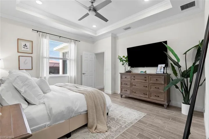 Bedroom with light hardwood / wood-style flooring, crown molding, ceiling fan, and a raised ceiling
