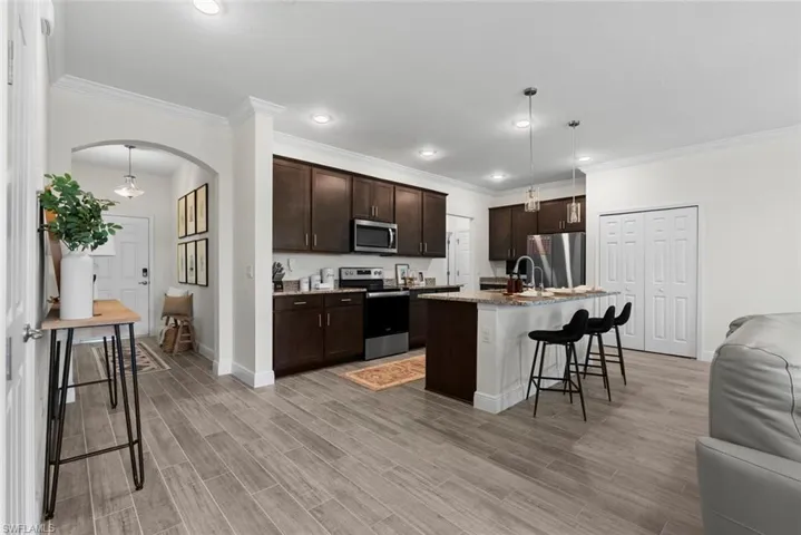 Kitchen with stainless steel appliances, a kitchen island with sink, a breakfast bar, ornamental molding, and decorative light fixtures