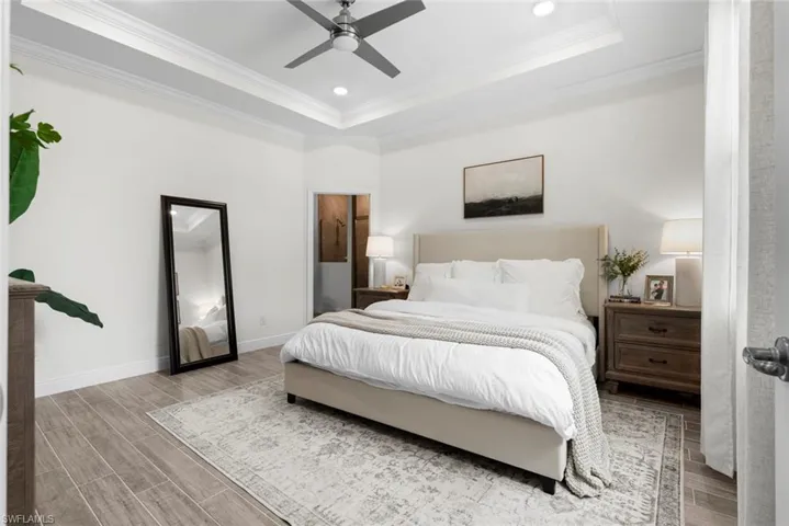 Bedroom with ceiling fan, light wood-type flooring, crown molding, and a tray ceiling