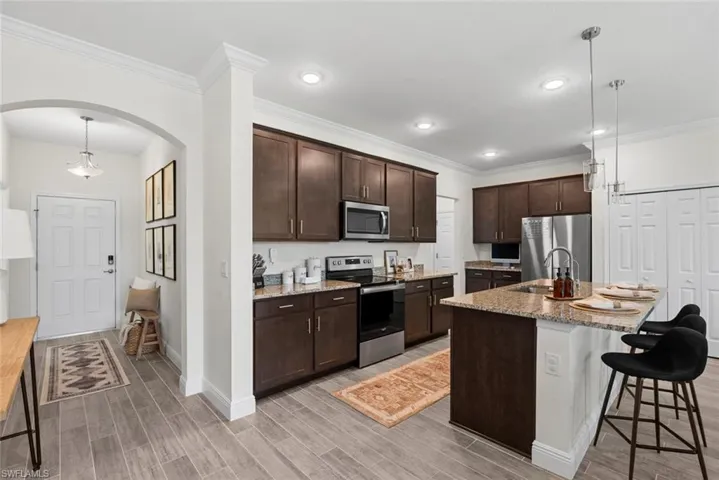 Kitchen with a breakfast bar, dark brown cabinets, an island with sink, stainless steel appliances, and sink