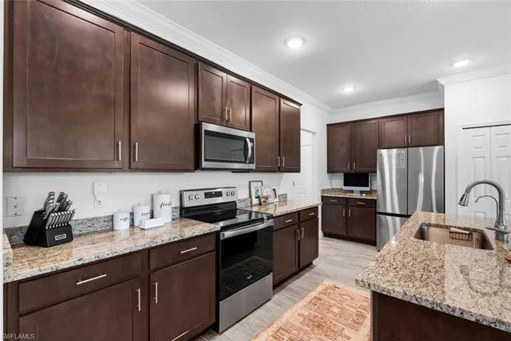 Kitchen with appliances with stainless steel finishes, dark brown cabinets, light wood-type flooring, and sink