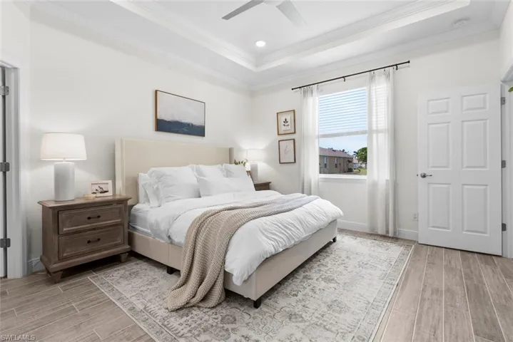 Bedroom featuring light hardwood / wood-style flooring, a tray ceiling, ornamental molding, and ceiling fan