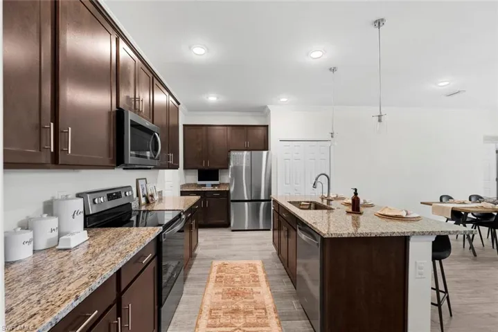 Kitchen featuring appliances with stainless steel finishes, light stone countertops, an island with sink, a breakfast bar area, and light wood-type flooring