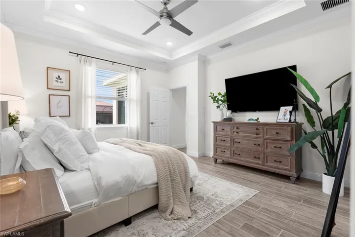 Bedroom featuring light wood-type flooring, crown molding, ceiling fan, and a raised ceiling