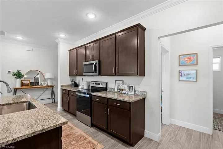 Kitchen with crown molding, appliances with stainless steel finishes, light stone countertops, sink, and dark brown cabinetry