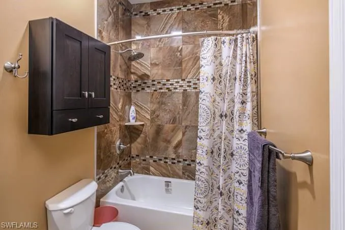 Bathroom with toilet and shower / bathtub combination with curtain