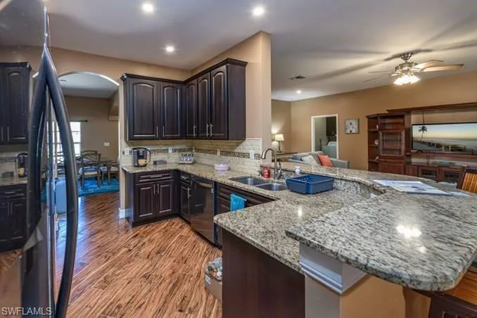 Kitchen with light stone countertops, sink, dishwasher, kitchen peninsula, and light wood-type flooring
