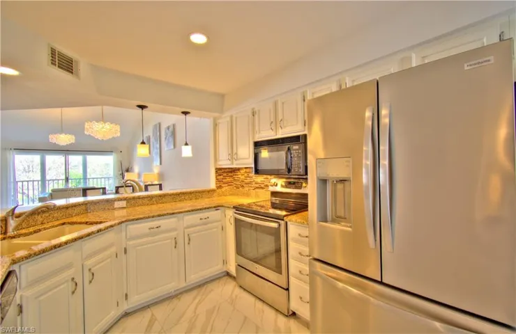 Kitchen featuring stainless steel appliances, white cabinetry, light stone counters, backsplash, and a chandelier